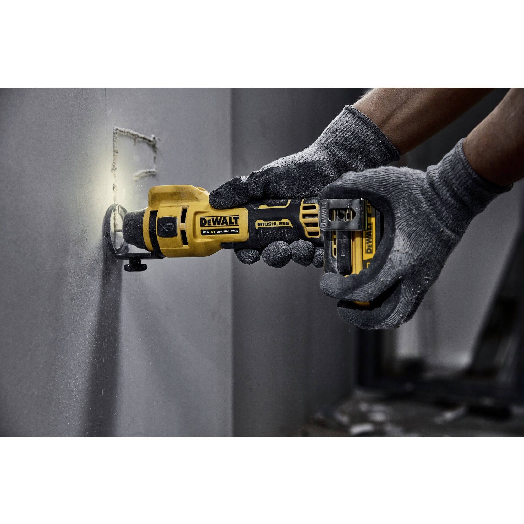 A person wearing gloves is using a yellow electric reciprocating saw to cut a hole in a grey wall.