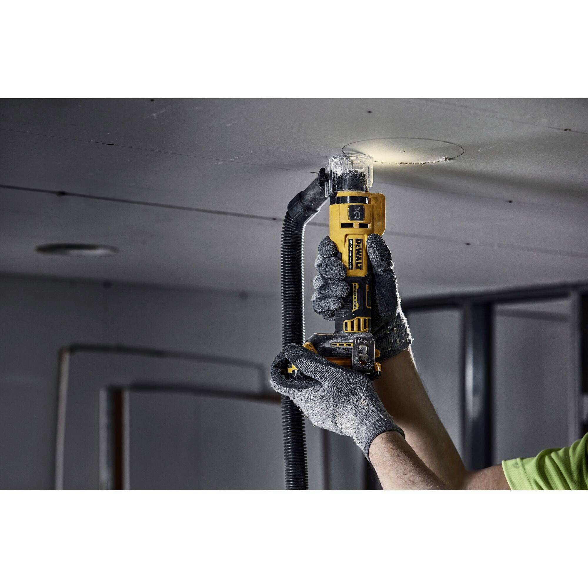 A person is cutting a round hole in a ceiling using an oscillating tool while wearing protective clothing.