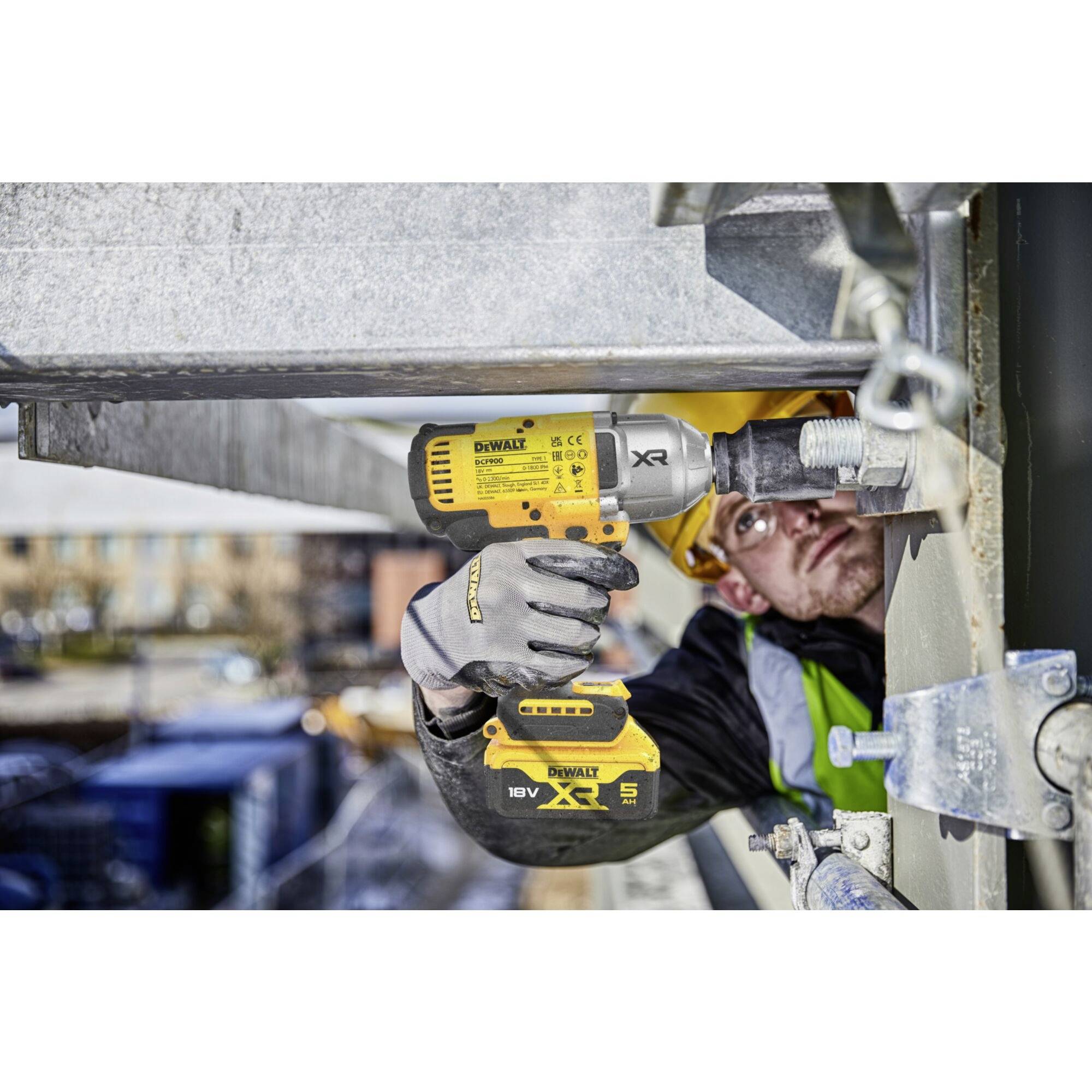 A construction worker tightens a screw with a cordless drill on a building site. He is wearing safety clothing and a hard hat.