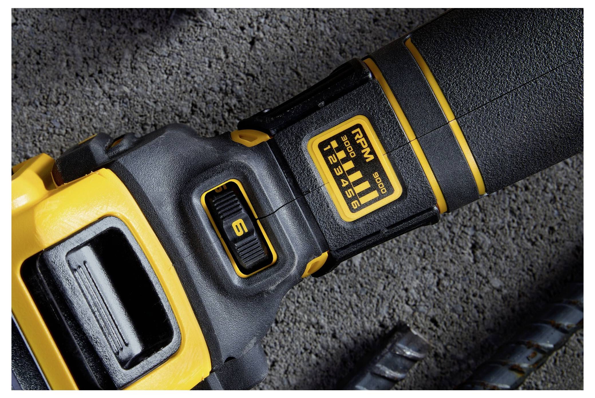 Close-up of a yellow and black electric power tool on a concrete surface. The tool shows a speed control dial with a scale from 1 to 6.