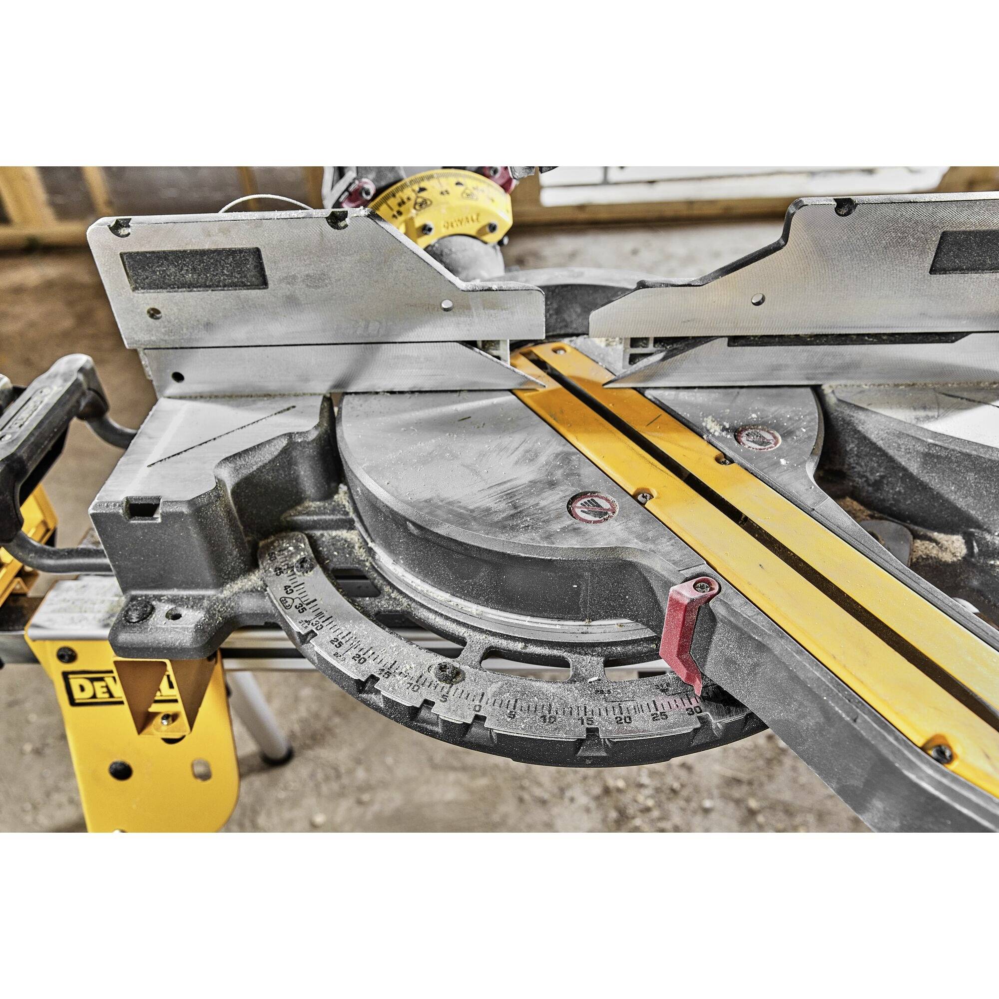 Mitre saw on a construction site, ready for wood cutting; scale indicates angle, yellow guide rail for precision; concrete floor in the background.
