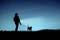 A person is walking with a dog on a lead, holding a torch. They are in a dark landscape at night.
