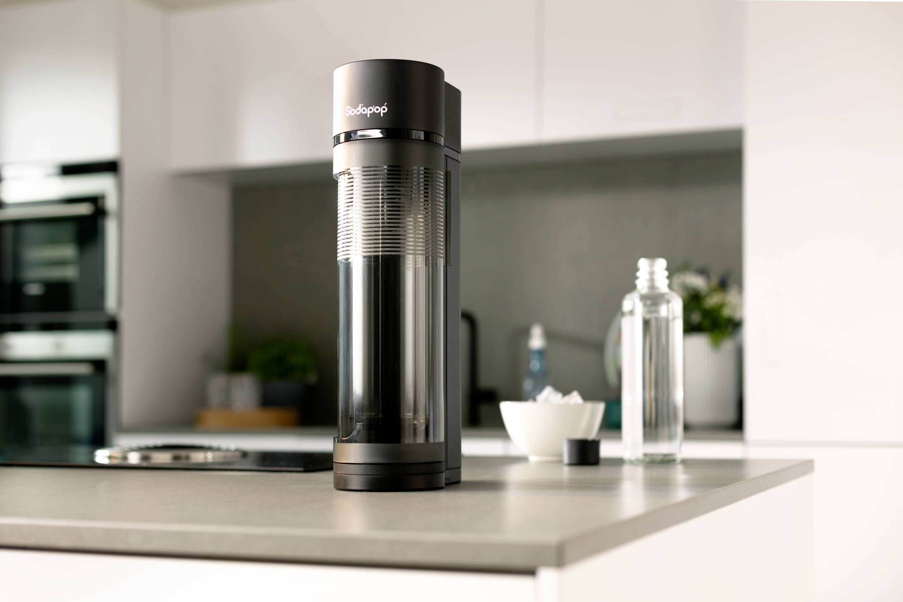 SodaStream sparkling water maker on a kitchen worktop. Bottles and a bowl in the background.