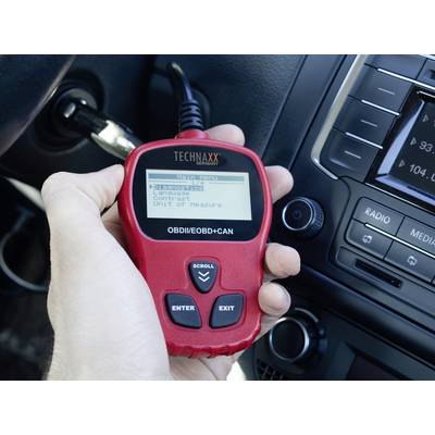 A person is holding a car diagnostic device that is connected to the vehicle. Menu options are displayed on the screen.