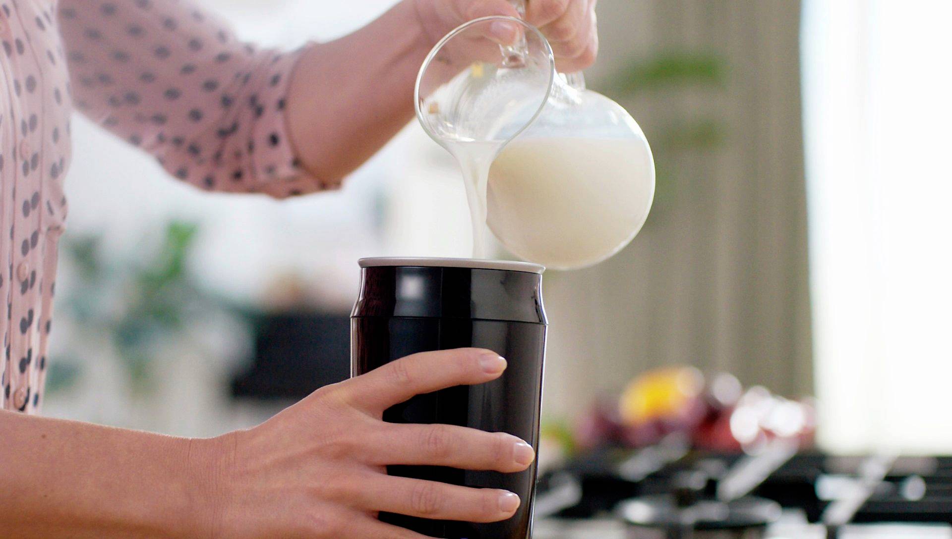 A person is pouring milk from a small jug into a black mixing bowl in a kitchen scene.