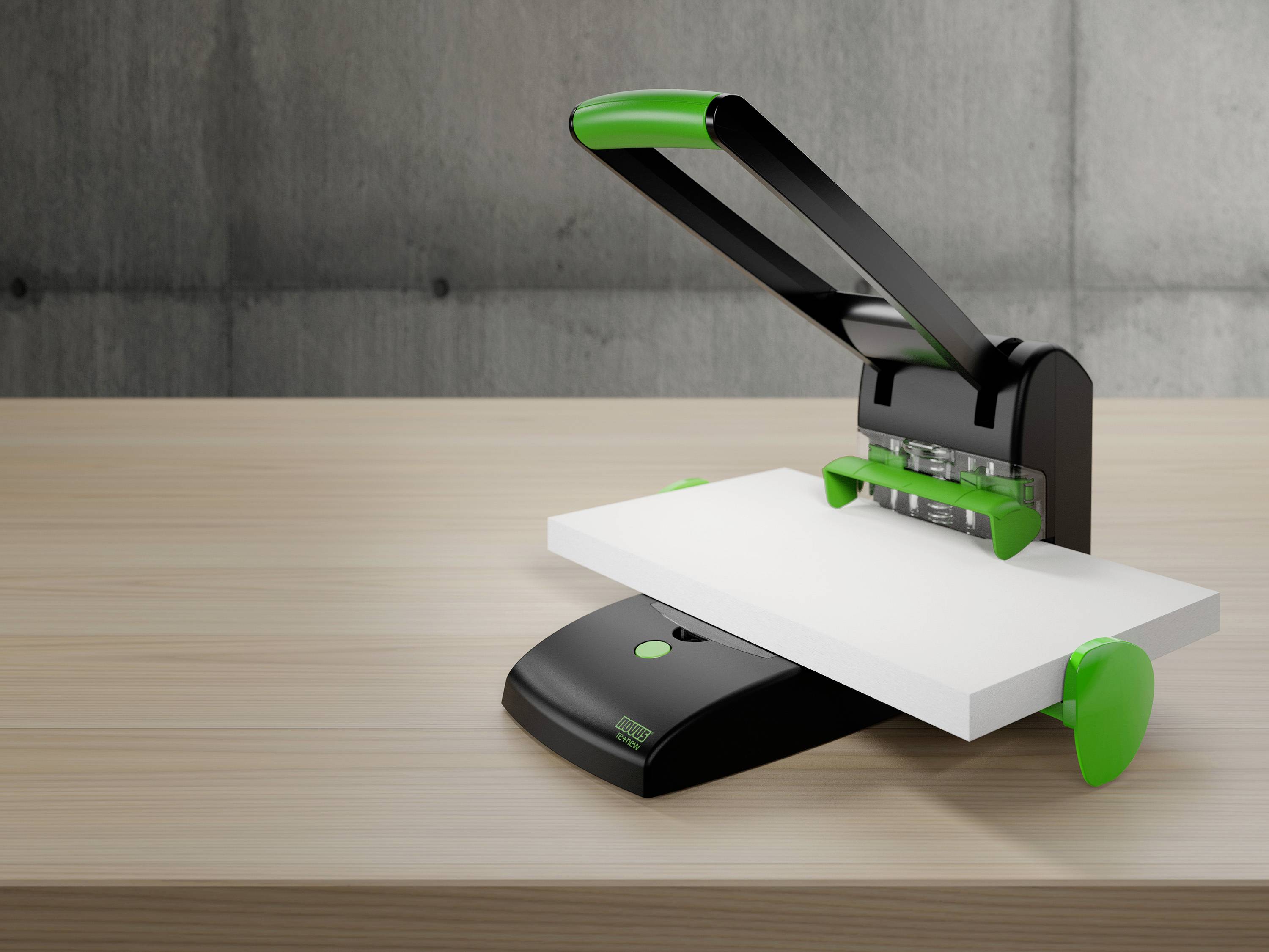 Hole punch on a wooden table, black casing with a green lever and green details, suitable for stacks of paper.