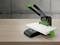 Hole punch on a wooden table, black casing with a green lever and green details, suitable for stacks of paper.