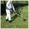 A person in protective clothing uses a grass trimmer to cut overgrown grass in a garden, surrounded by greenery.