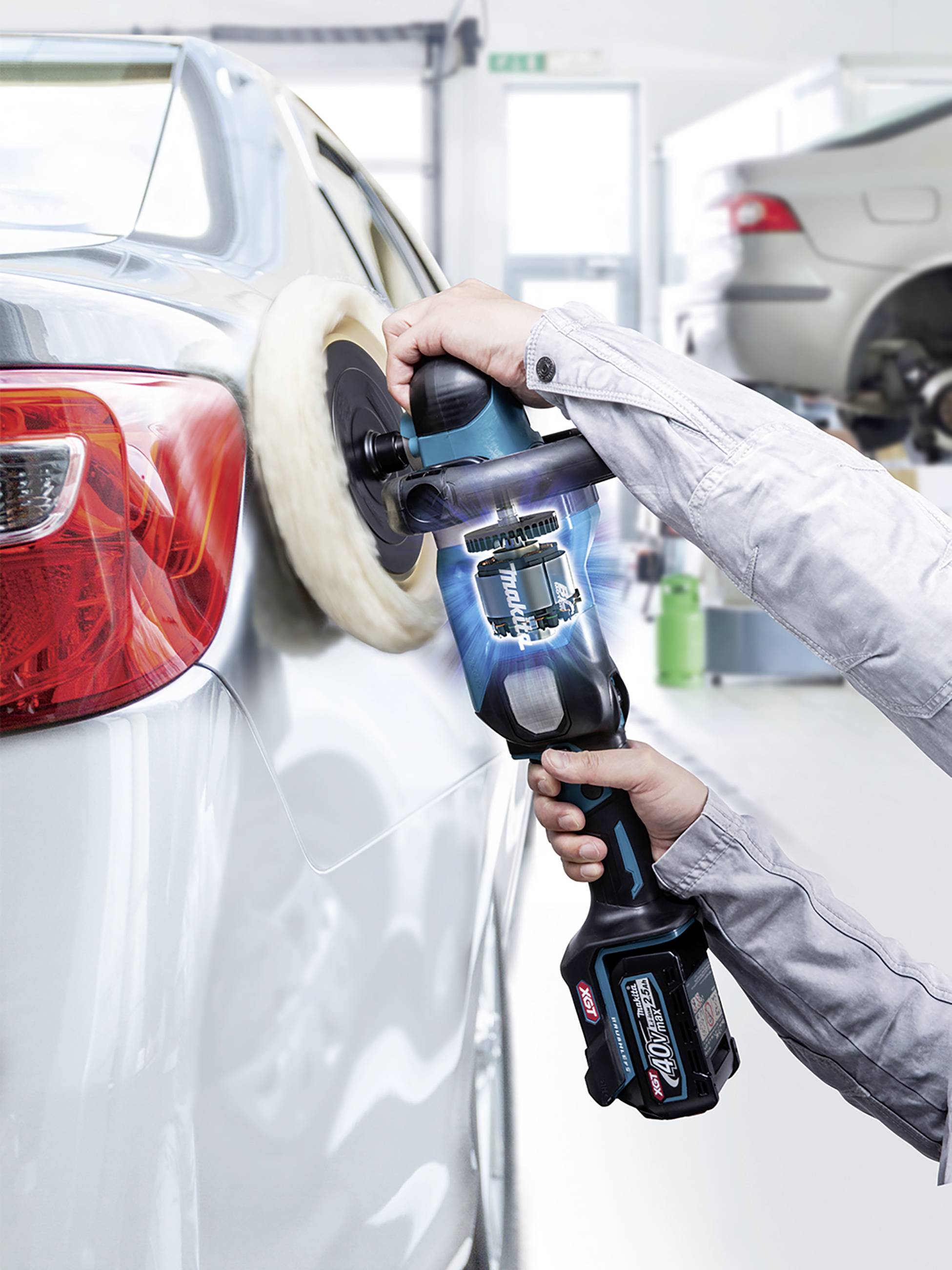 A person is polishing the shiny surface of a car with an electric polishing machine in a car workshop.
