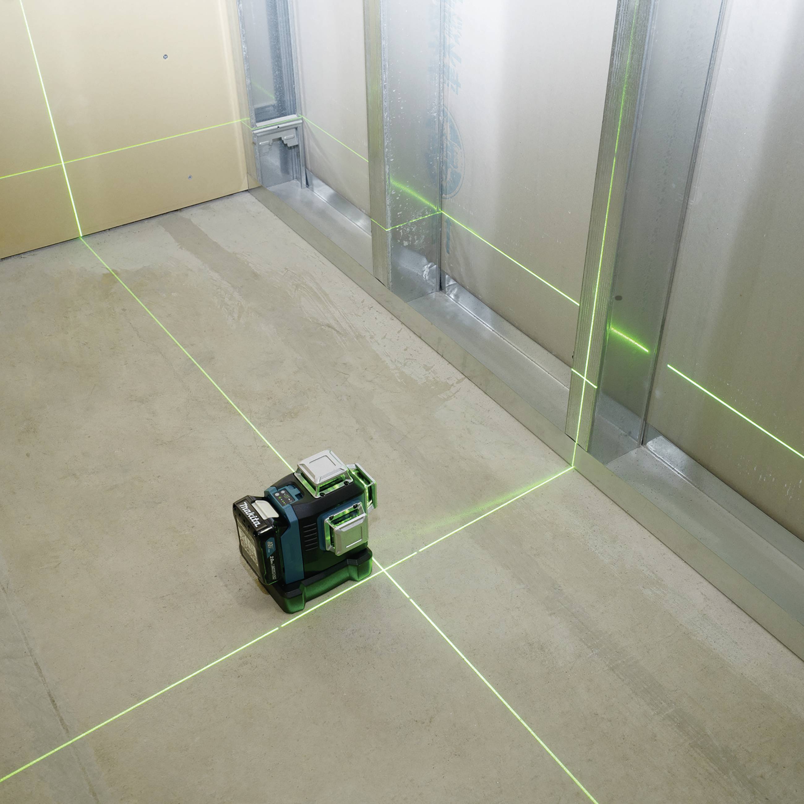 A green laser level projects horizontal and vertical lines onto a wall and floor in a room to enable precise measurements.