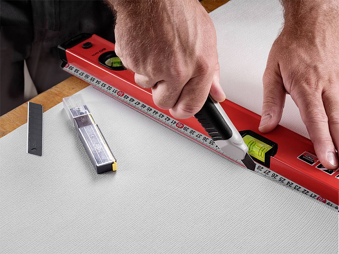 A person is cutting along a ruler with a craft knife on a linen cloth.