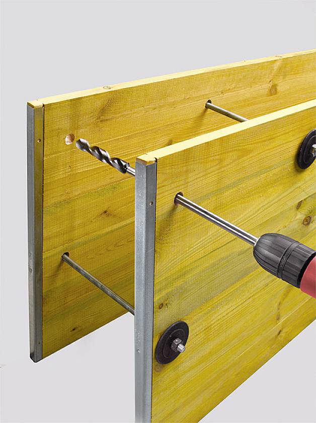 'Two yellow wooden planks are connected with metal rods. A drill is loosening a screw on one of the planks.'
