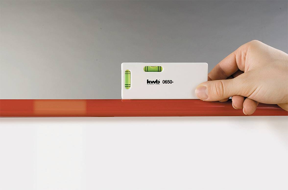 A hand is holding a spirit level on a red beam to check its alignment.