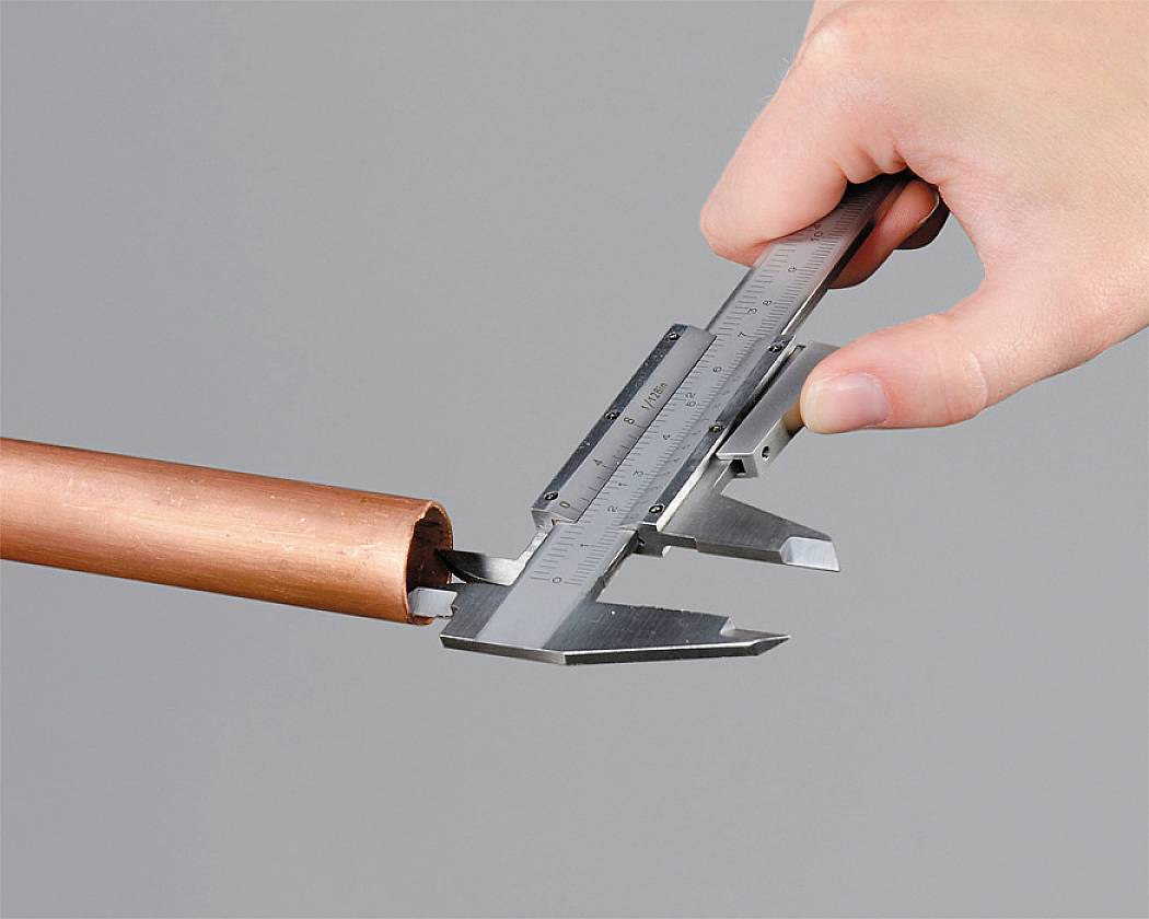 A hand is holding a calliper measuring the diameter of a copper pipe.
