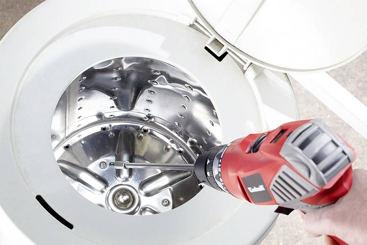 A red drill is used to secure a screw inside the drum of a washing machine.