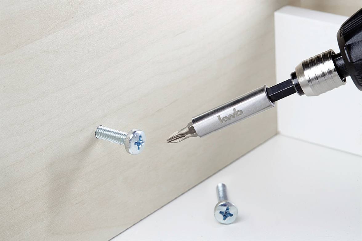 A screwdriver is used to screw a screw into a wooden board. Other screws are visible in the background.