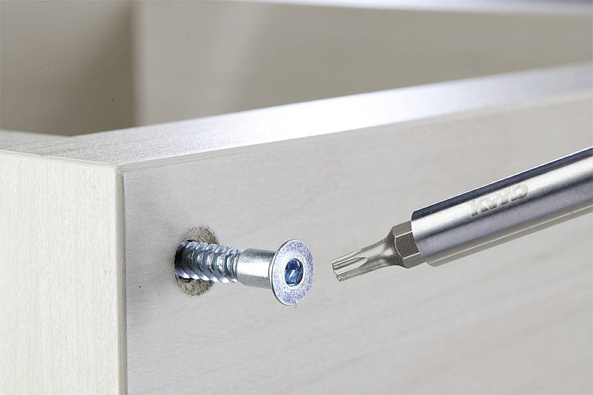 A screwdriver is driving a screw into a wooden board.