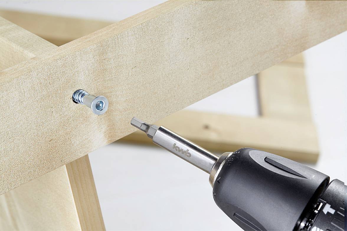 A close-up shows a wooden structure with a screw being driven in using an electric screwdriver.