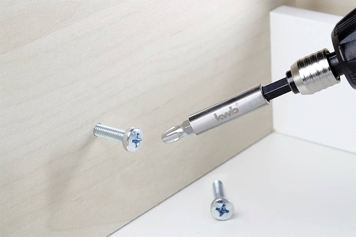 A screwdriver in a drill is driving a screw into a wooden board; two additional screws are visible.