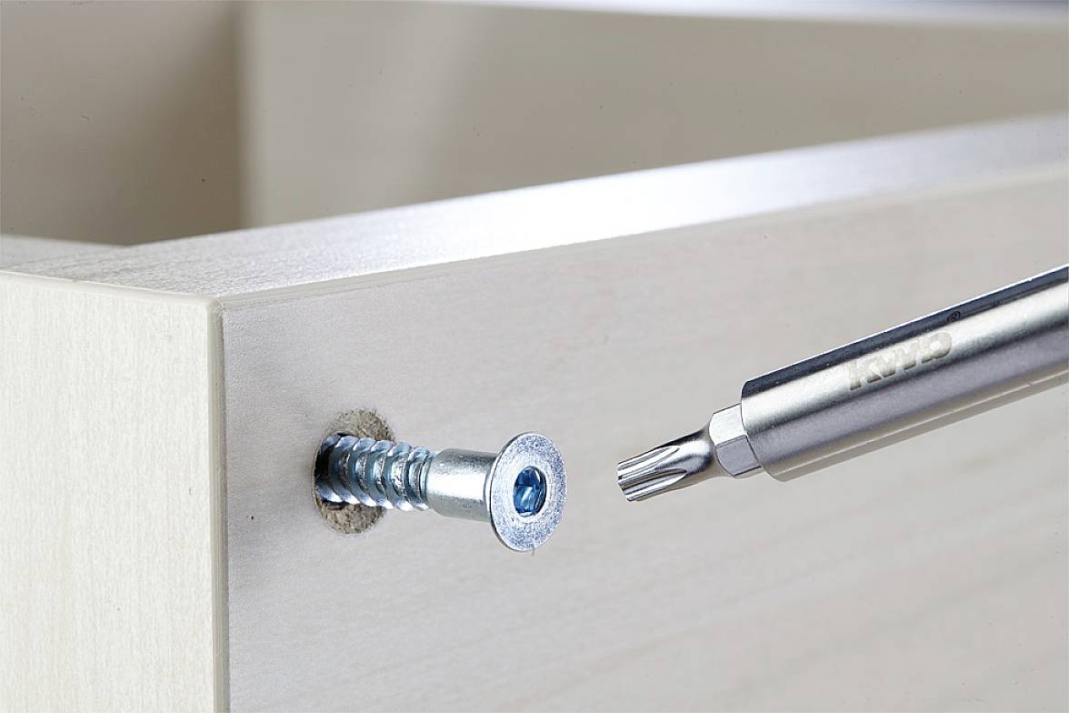 A metal pin is used to screw a screw into a wooden board.