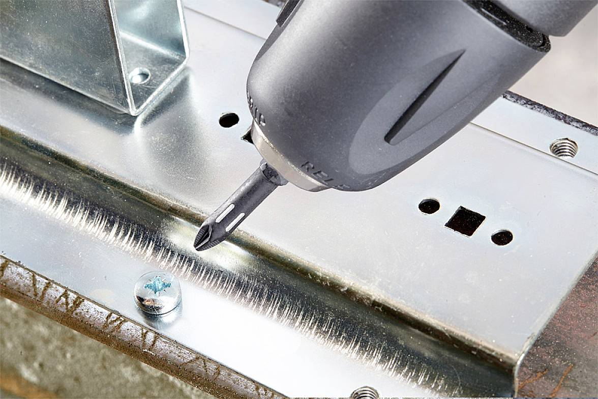 Cordless drill driving a screw into a metal plate, demonstrating metalwork craftsmanship.