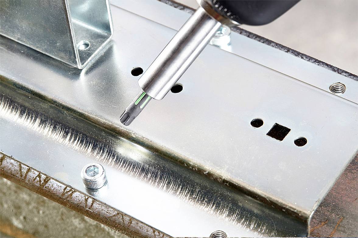 Close-up of an electric screwdriver turning a screw into a metal component. The main focus is on the tool and the screwing process.