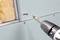 A cordless drill with a screwdriver attachment is ready to screw a screw into a plasterboard wall with visible insulation.
