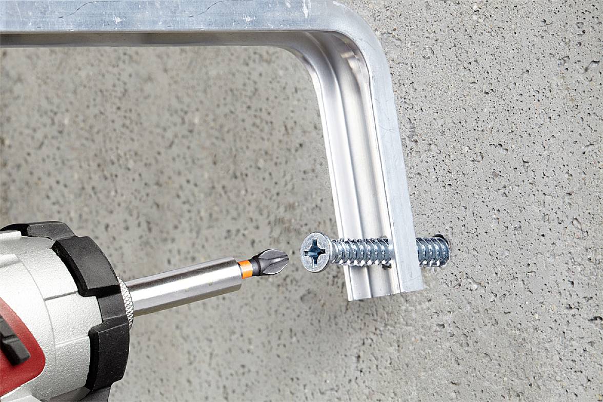 A screwdriver is securing a screw in a metal bracket mounted on a concrete wall.