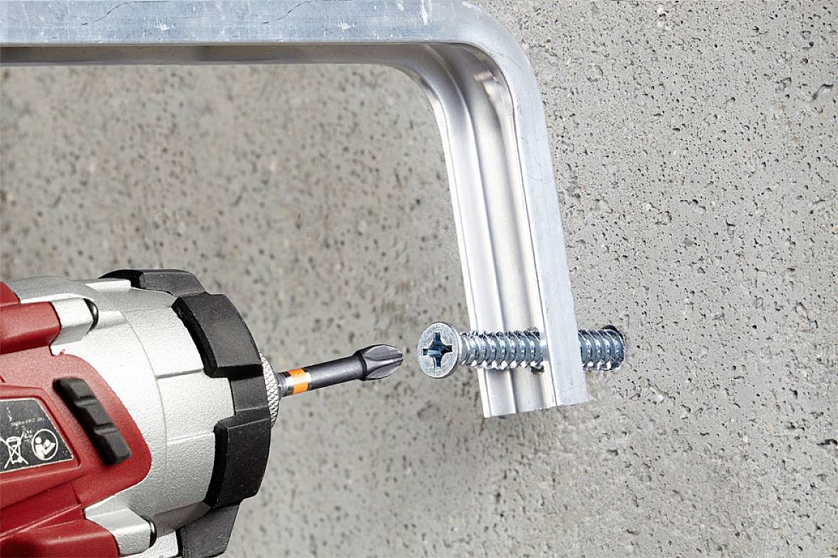 Cordless drill drives screw into metal bracket secured to concrete wall.