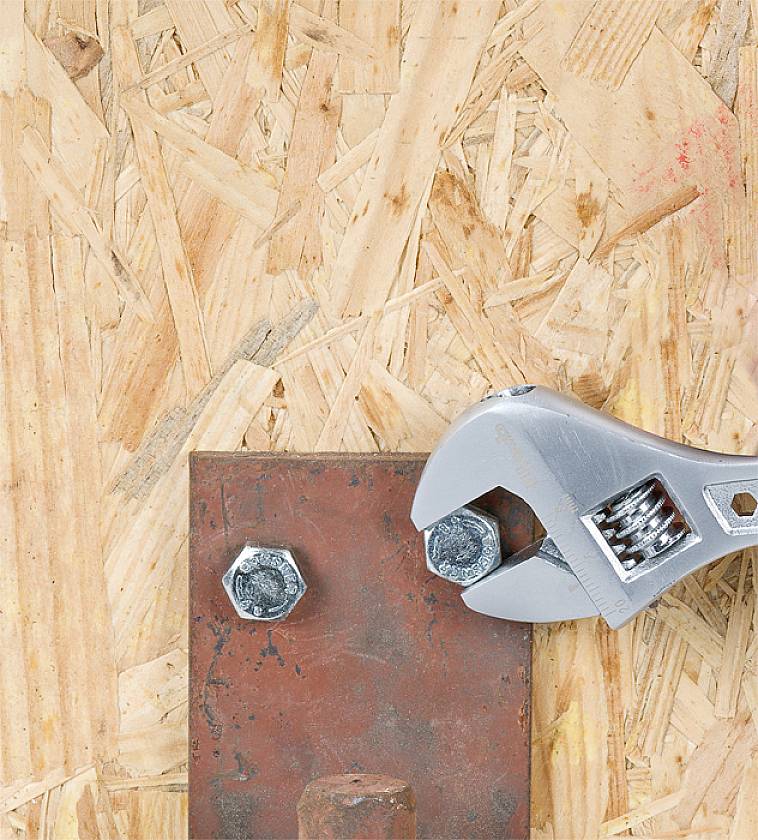A spanner tightens a nut onto a rusty metal piece lying on plywood.