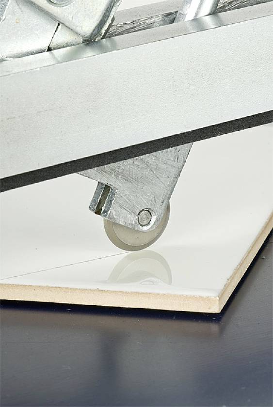 Close-up of a furniture castor with a grey wheel rolling over a glossy white surface, with a black surface underneath.