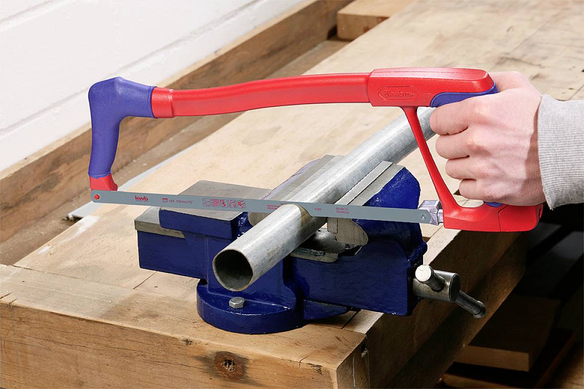 A person is sawing a metal pipe with a metal saw, which is secured in a vice on a workbench.