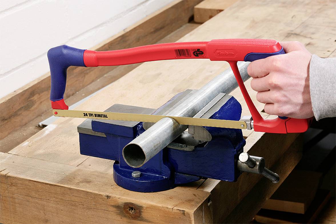 A person is sawing a metal pipe clamped in a vice using a hacksaw.