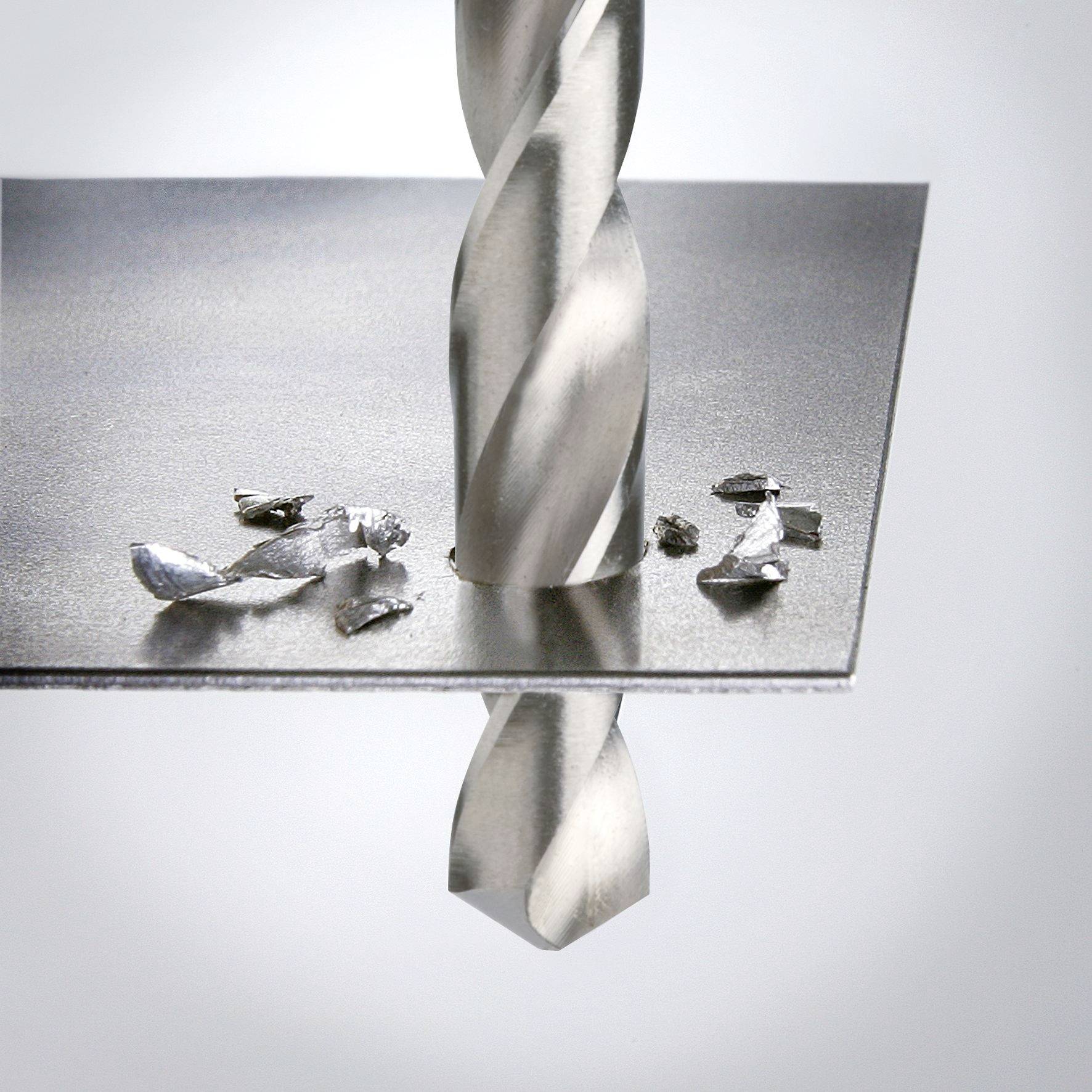 A drill penetrates a metal sheet, surrounded by small metal shavings.