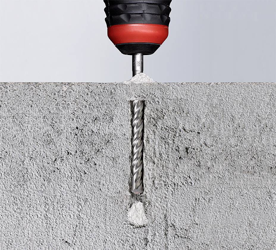 A drill penetrates a concrete wall, creating dust and debris. At the top, half of the red drill head is visible.