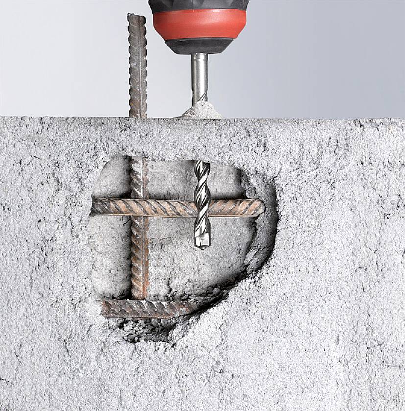 'Drill penetrates a concrete wall, revealing a metal grid behind it.'