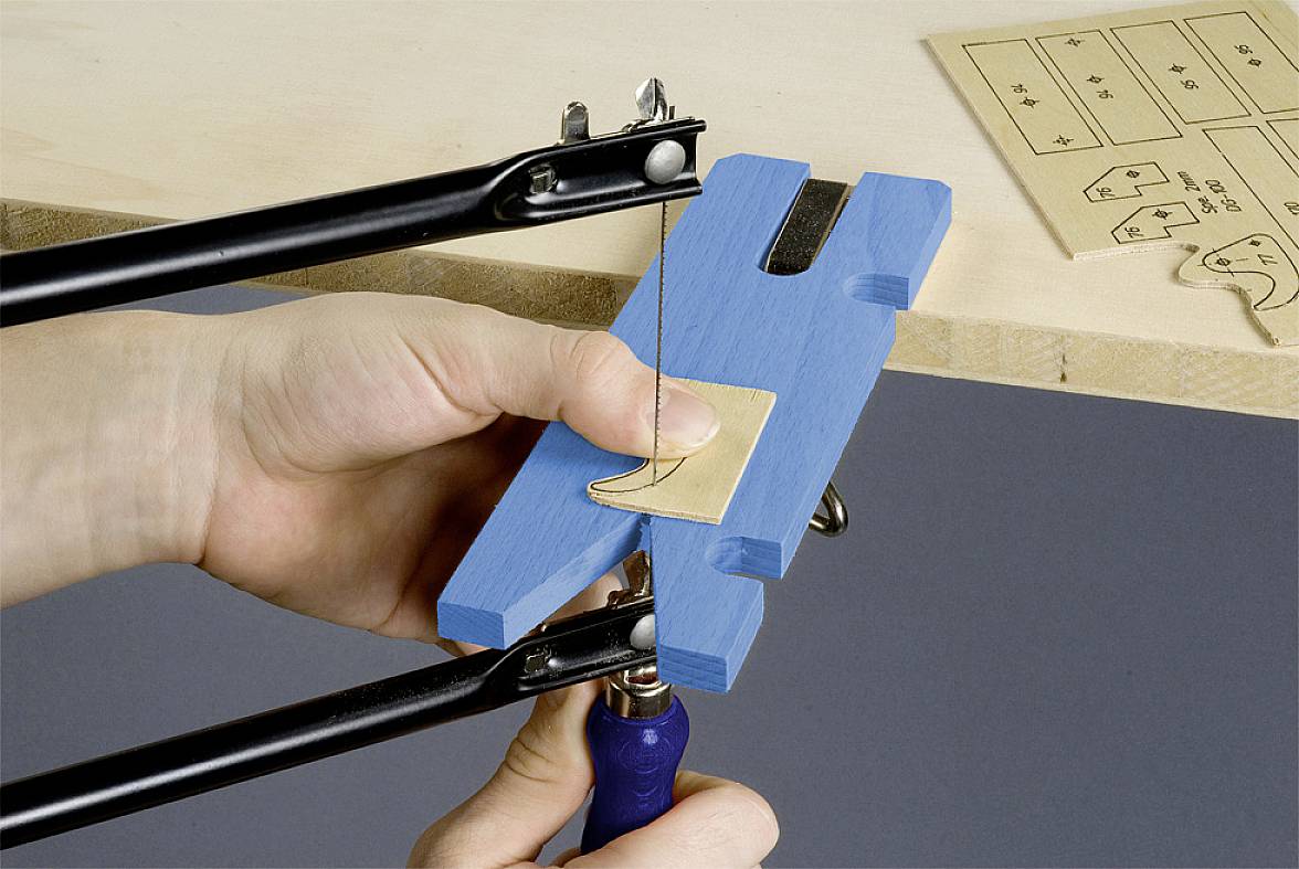 A person is cutting wood with a fretsaw, using a clamp to secure the material.
