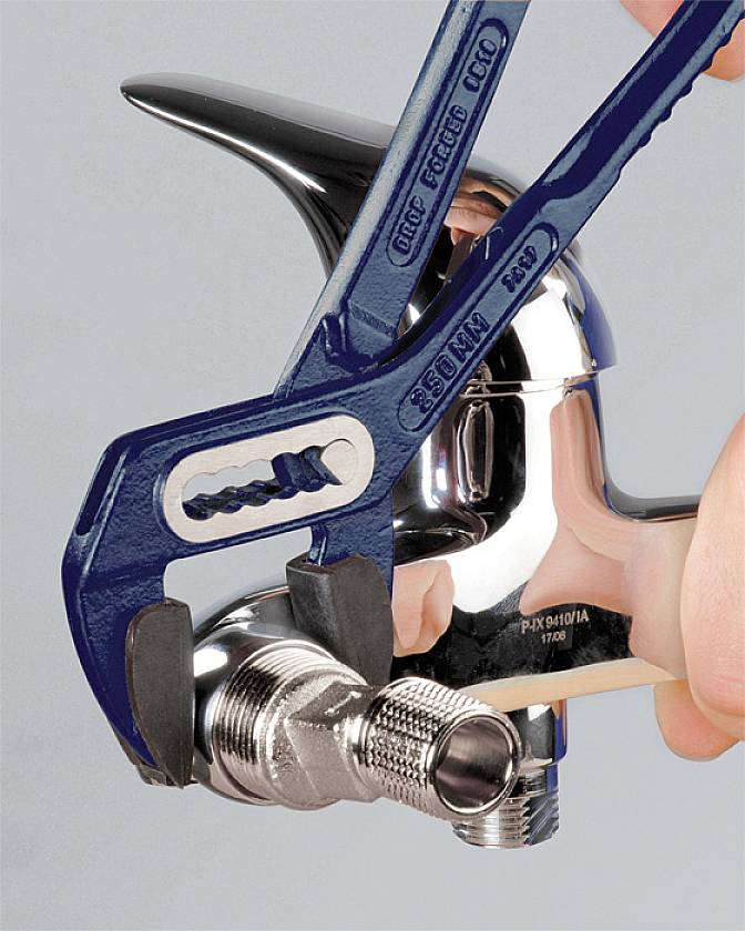 A pipe wrench adjusts a tap. A finger points to the connection. The tap is gleaming and shown in a close-up.