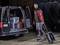 A man pulls a toolbox on wheels in front of an open van that has several toolboxes loaded. It is dark.