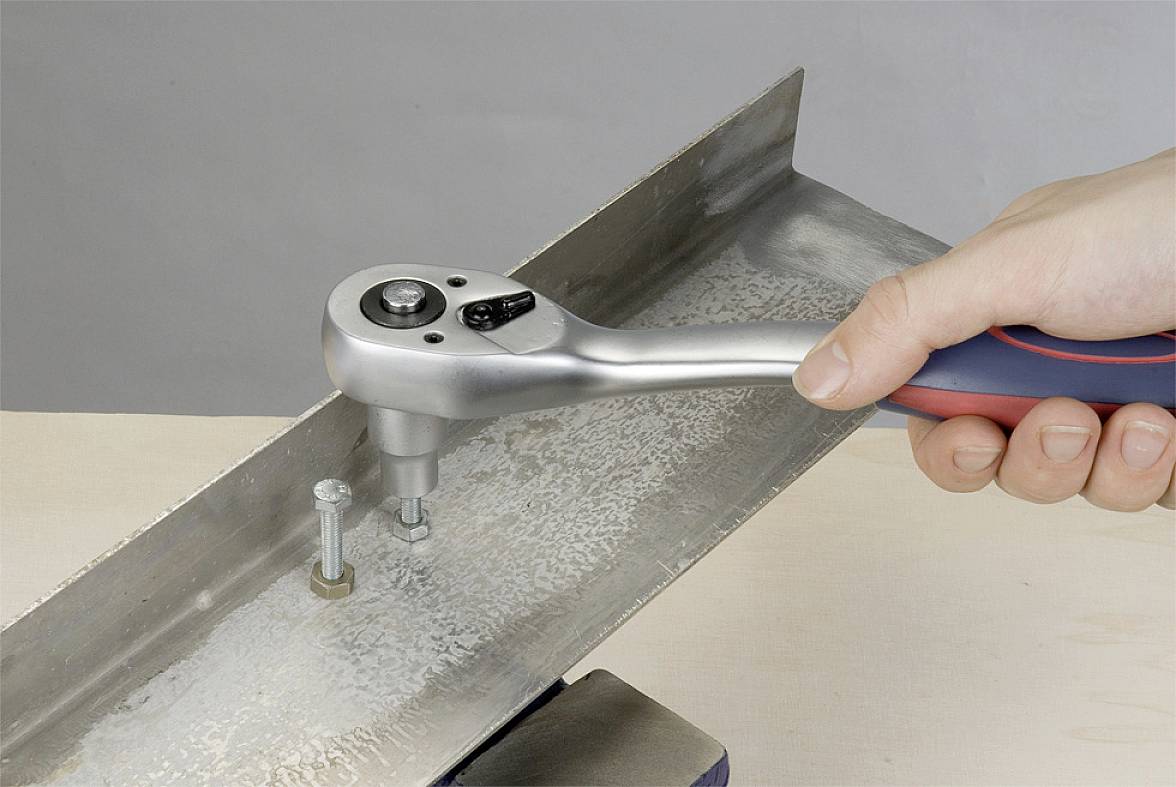A hand is using a ratchet spanner to screw a bolt into a metal angle bracket.
