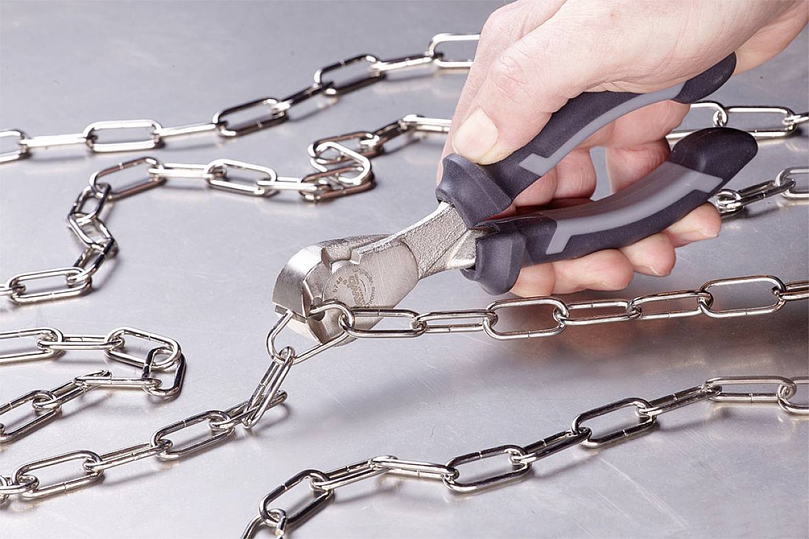 A hand is holding pliers about to cut through a metal chain on a table.
