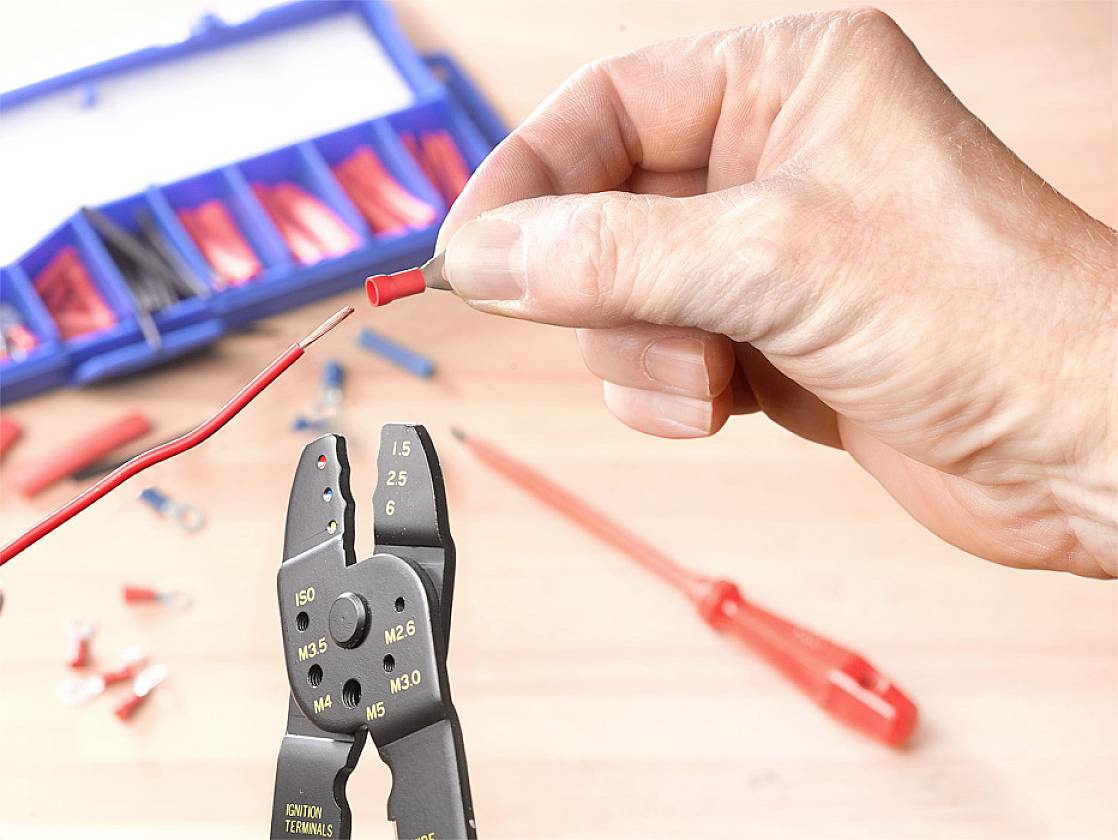 A hand is holding an insulated cable connection, while another hand is using wire strippers with a clamped wire.