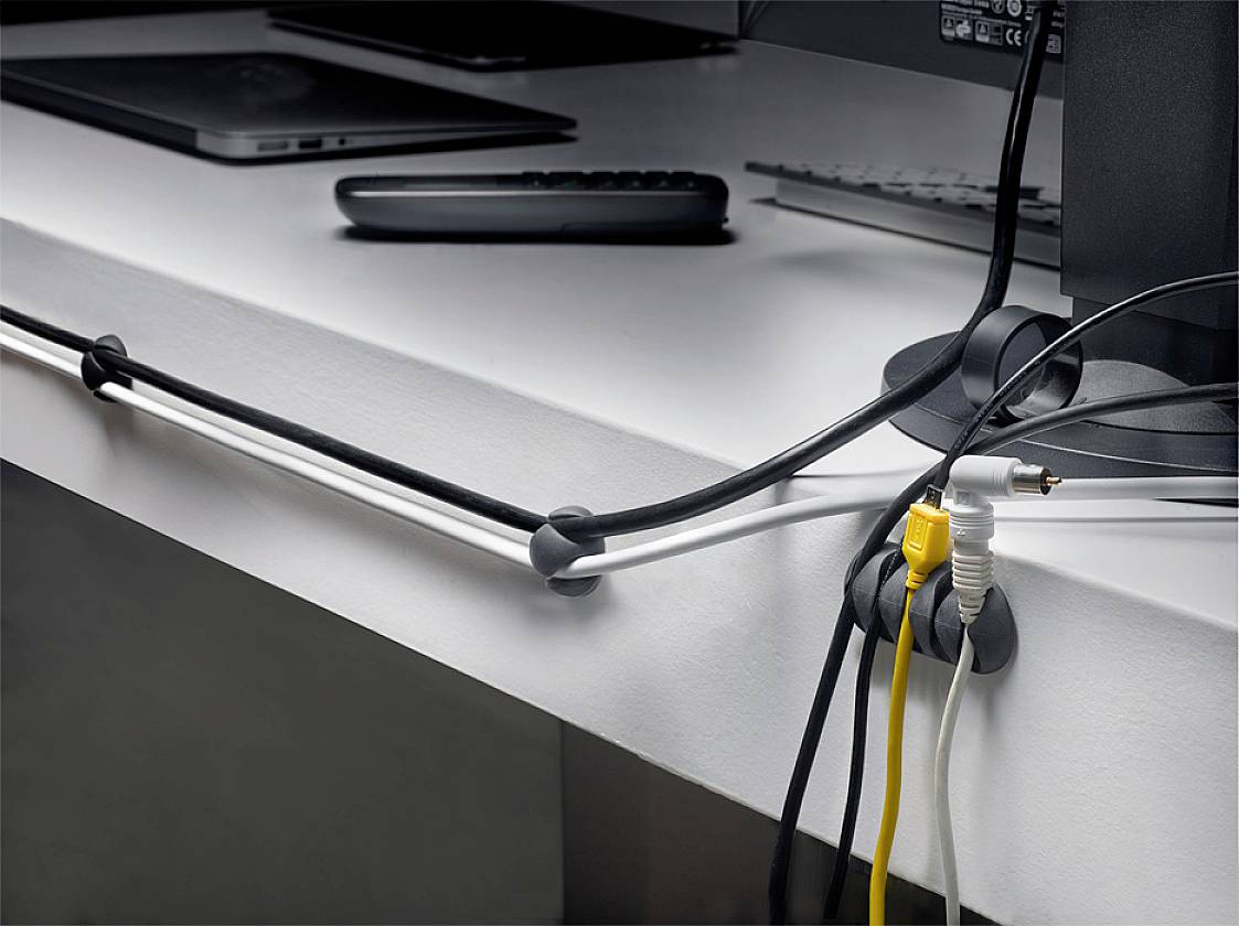 Cable management on a desk with multiple cables neatly secured to cable clips to create order.