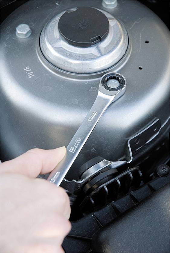 A hand is holding a spanner to tighten a nut on a mechanical component of a car.