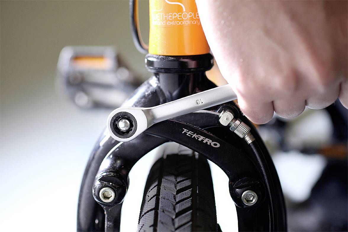 A bicycle mechanic tightens a screw on the front wheel brake of a bicycle using a spanner.