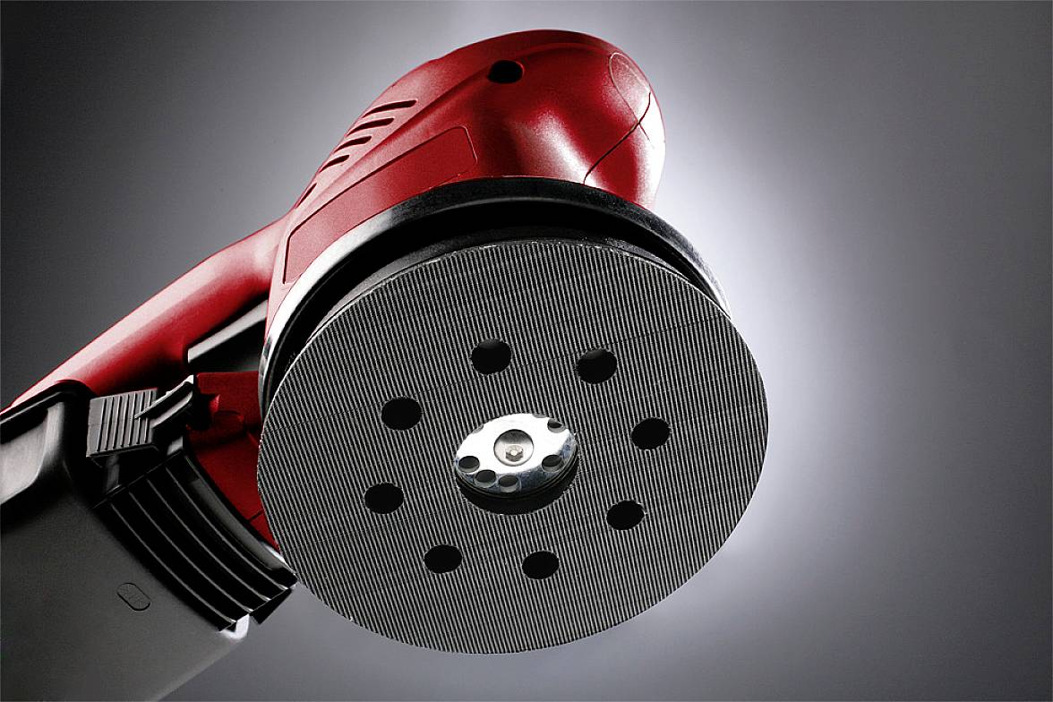 A red orbital sander with a circular sanding head against a grey background, used for surface processing.