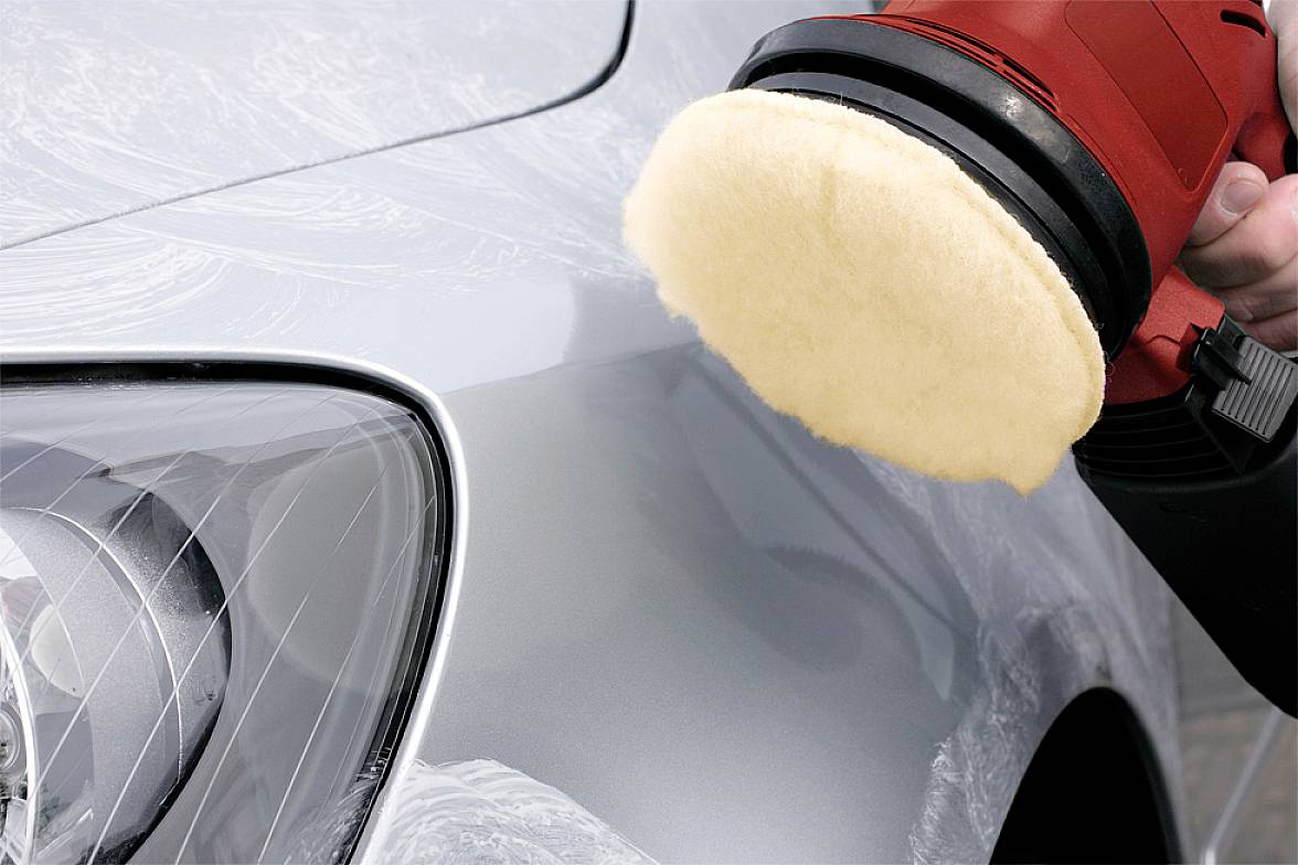 A polishing machine is being used to polish the paintwork of a silver car, with the front vehicle headlight visible.