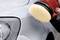 A polishing machine is being used to polish the paintwork of a silver car, with the front vehicle headlight visible.