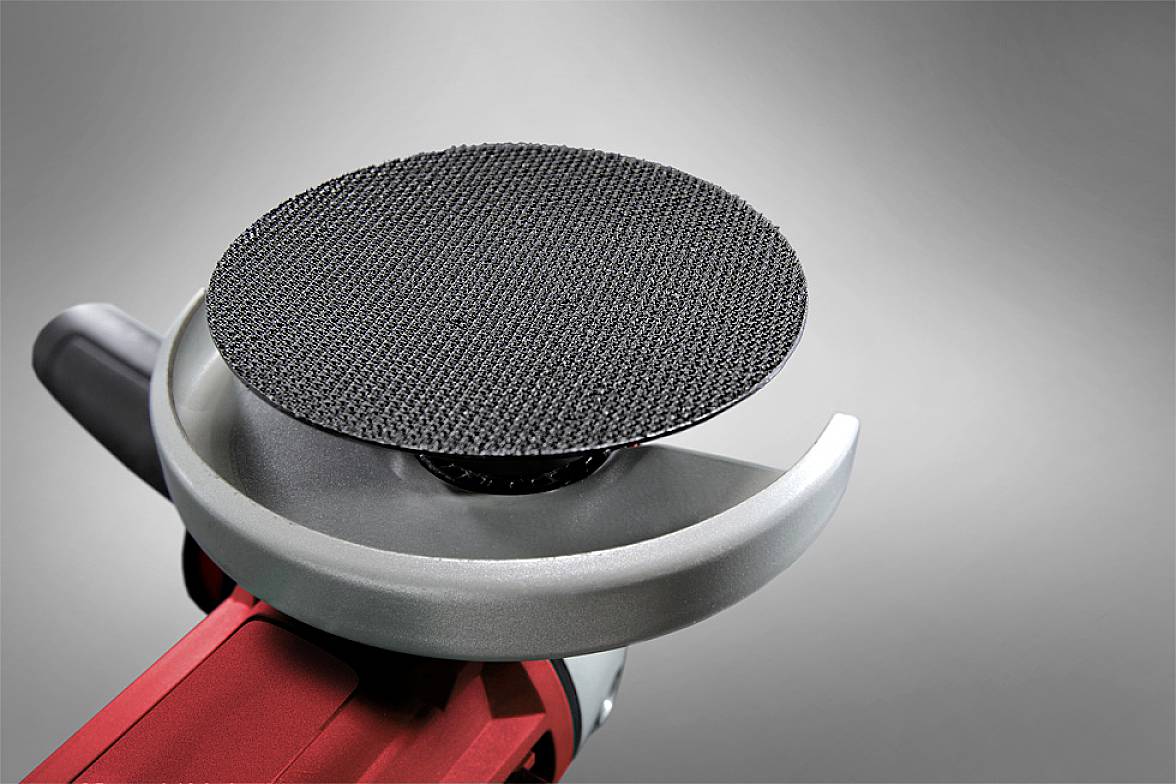 An angle grinder with an attached grinding disc on a grey background. Tool in close-up without direct use.