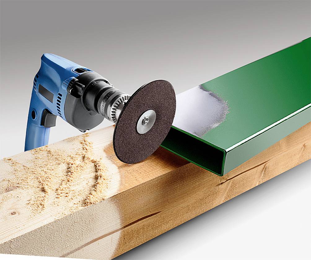 A blue drill with a grinding wheel is processing the surface of a wooden beam next to a green metal profile.